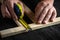 Professional carpenter or woodworker uses a construction tape to measure length of a piece of wood. Hands of the master close-up