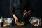 The professional chef beats eggs with a whisk in glass bowl for preparing dough. Dark background. Bakery concept