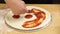 A professional chef lays out the sauce on the pizza dough.