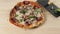 Professional chef places fresh green basil leaves on top of salami pizza to enhance the taste. Concept of cooking delicious pizza