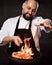 Professional chef prepares the dish with flame stirring in a frying pan on kitchen of the restaurant