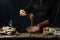 The professional chef testing dough for preparing waffles on rustic wooden table with ingredients on dark blue background.