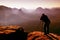 Professional on cliff. Nature photographer takes photos with mirror camera on peak of rock. Dreamy blue fogy landscape,