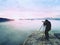 Professional on cliff. Nature photographer takes photos with mirror camera on peak of rock. Dreamy fog