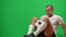 Professional confident footballer juggling catching ball with legs sitting on green screen and looking away smiling