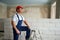 Professional construction worker in uniform standing with spatula on step ladder. Portrait of contractor in hardhat