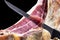 Professional cutter carving slices from a whole bone serrano ham. Knife cutting a spanish serrano ham. Hands of a chef cutting tra