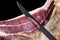 Professional cutter carving slices from a whole bone serrano ham. Knife cutting a spanish serrano ham. Hands of a chef cutting tra