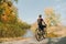 Professional cyclist in helmet and sportswear stands with bicycle, background of lake and autumn park and admiring the landscape,