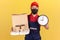 Professional delivery man in uniform and protective mask holding wall clock and coffee with pizza box, express delivery in time,