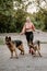Professional dog walker exercising two dogs in park. Young woman with dogs outdoors. Fitness girl walking two German shepherds