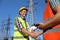 Professional electricians shaking hands near high voltage tower