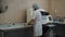 Professional female assistant dressed in white lab coat, protective mask, cap and latex gloves bringing rack of test