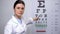 Professional female optometrist showing letters on eye chart, sight examination