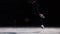 A professional figure skater performs ice skating with a jump in the air with a black background in a black suit. Ice