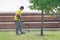 Professional gardener using an edge trimmer in the city parck. Elderly man worker mowing lawn with grass trimmer outdoors on sunny