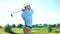 Professional golfer hitting ball in swing position, looking at meadow, sport