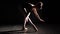 Professional graceful flexible ballerina standing on her pointe ballet shoes in spotlight on black background in studio