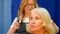 Professional hairdresser stylist is doing hairstyle for senior blonde woman, front view.