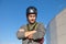 A professional in a hard hat confidently looks at the camera with his arms crossed on his chest. A European worker on a sunny day