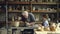 Professional male potter is working with clay on spinning throwing-wheel with his curious grandson helping him. Ceramic