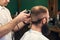 Professional male short haircutting for bearded client in barbershop. Young barber working with electric razor. Close up