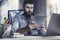 Professional at office desk using tablet in his work.Dark-haired man sitting at window in front of laptop with tablet in his hands