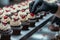 Professional pastry chef hands with black gloves decorating cupcakes with cream cheese cream and small red hearts