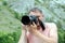 A professional photographer without clothes is looking into the viewfinder of a digital SLR camera. Adult man in glasses takes