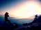 Professional photographer takes photos with mirror camera on peak of rock. Dreamy fogy landscape, spring orange pink misty sunrise