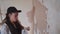 Professional plasterer female spackles the wall, applies and spreads plaster on a spatula in overalls and ball cap