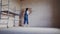 Professional plasterer female spackles the wall, applies and spreads plaster on a spatula in overalls and ball cap