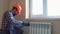 Professional plumber in a hard hat and gloves installing radiator in a room