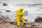 Professional in protective coveralls with mini lab on contaminated rocky sea shore