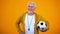 Professional proud aged trainer with football posing on camera, sport career