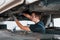Professional repairman in black shirt works under broken automobile