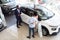 Professional Salesman Advertising New Car For Young Black Customers Couple In Showroom