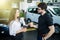 Professional salesperson selling cars at dealership to buyer while drinking welcome coffee