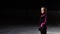 A professional skater stands on ice in ice skates and looks directly into the camera.
