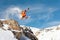 A professional skier makes a jump-drop from a high cliff against a blue sky leaving a trail of snow powder in the