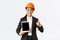 Professional smiling asian female construction manager, factory engineer in business suit and safety helmet showing