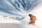 Professional snowboarder with a backpack leaving the cloud of snowy powder at sunset on a background of epic clouds and