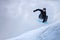 A professional snowboarder girl in flight after jumping from a snow eaves makes a rake against the gray sky on a cloudy