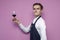 Professional sommelier holds a glass of red wine and looks at camera against a pink background, the guy the waiter checks the