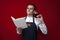 Professional sommelier holds a glass of red wine and reads a book on a red background, the guy looks at the menu and drinks wine