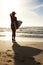 Professional surfer - Young woman looking at sea. Rear view of a young woman holding surfboard and looking at sea.