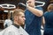 Professional tattooed barber making modern haircut for a young handsome guy sitting sitting barbershop chair. Focus on