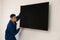 Professional technician installing modern flat screen TV on wall indoors