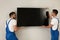 Professional technicians installing flat screen TV on wall indoors