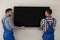 Professional technicians installing modern flat screen TV on wall indoors